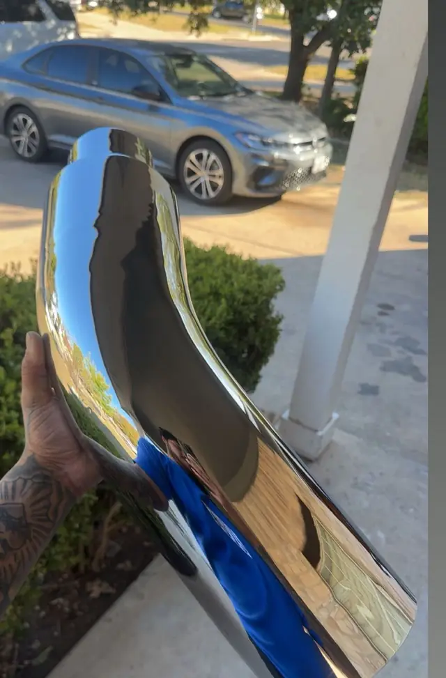 Polished chrome exhaust elbow held up outside the shop