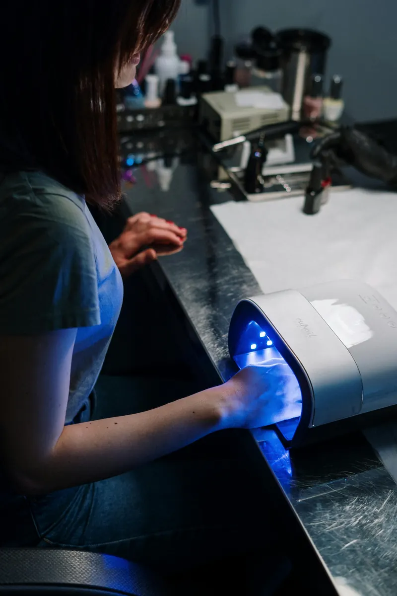 Clienta secando sus uñas de gel bajo la lámpara LED
