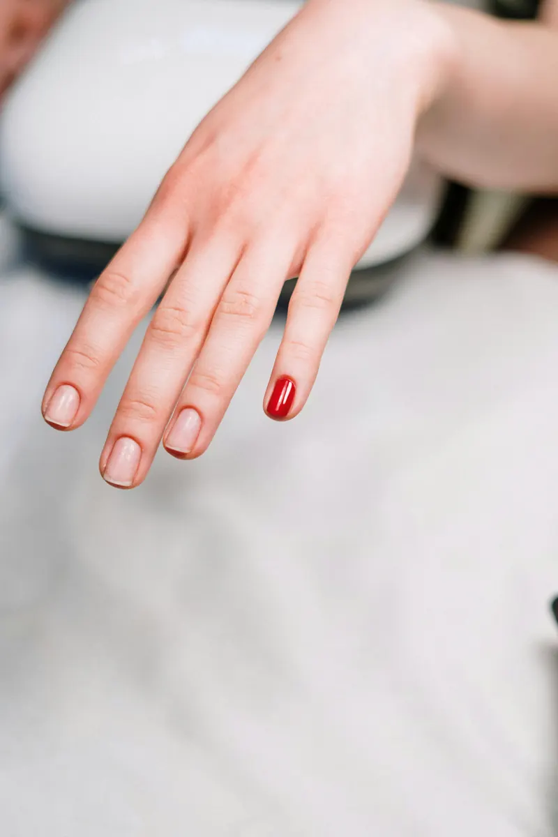 Mano con uñas cortas en tono nude y una uña en rojo