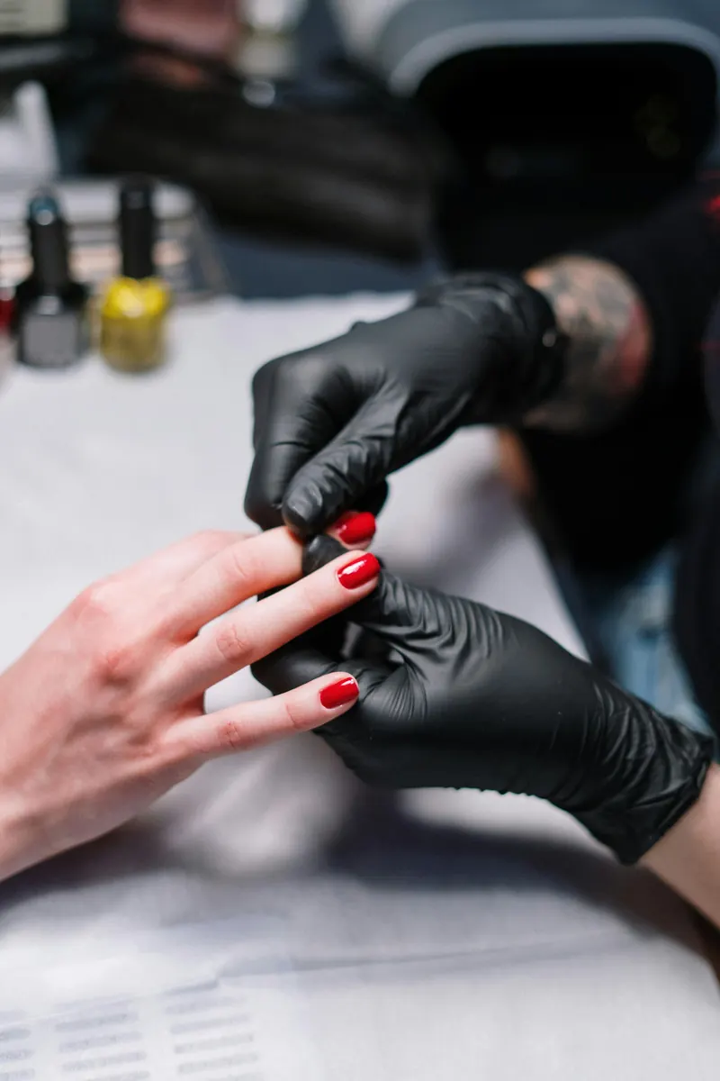 Manicurista aplicando esmalte rojo con guantes negros