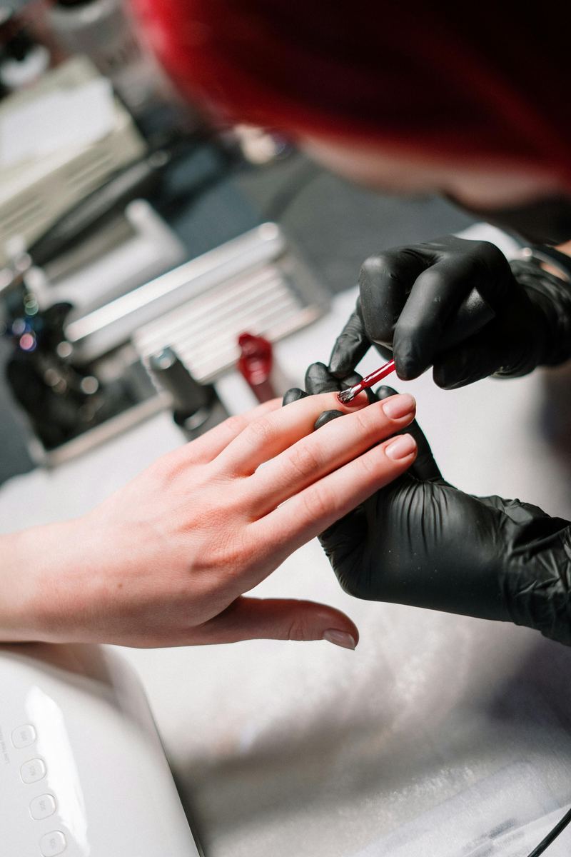 Manicurista con guantes negros aplicando esmalte a una clienta