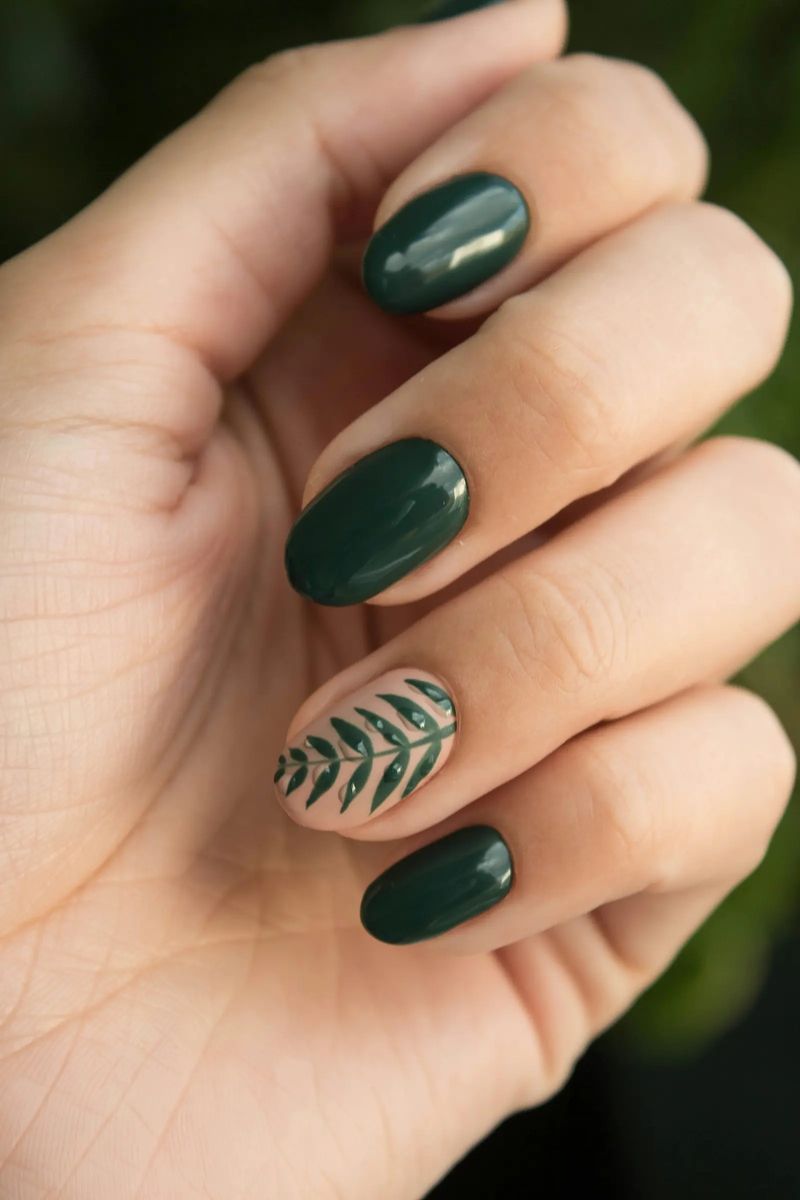 Manicura verde oscuro con una uña decorada con una hoja pintada a mano