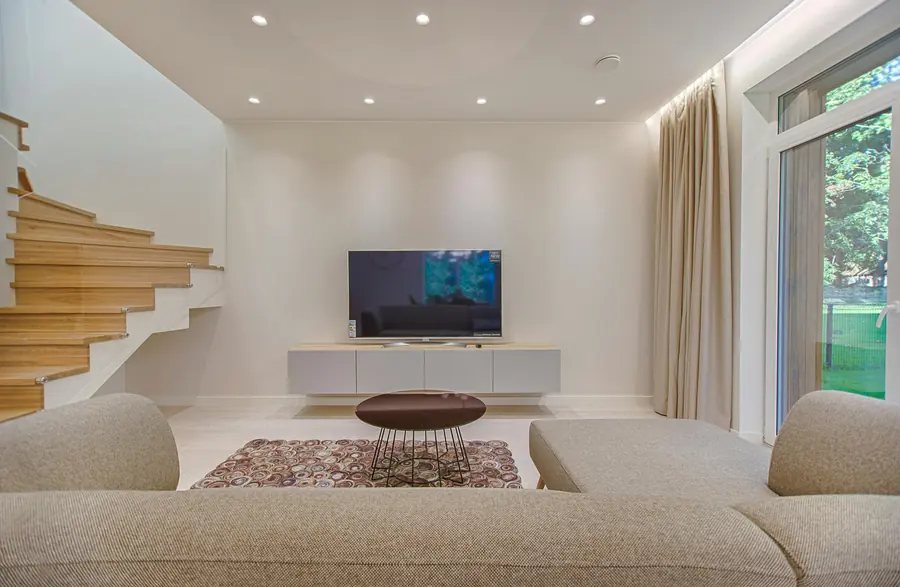 Sala amplia con sofá modular gris claro, mesa de centro de madera y ventanales al jardín