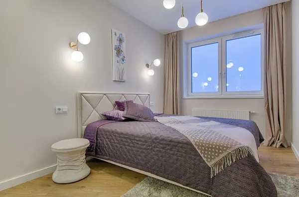 Cama king size con cabecera tapizada en tono crema y colcha lila
