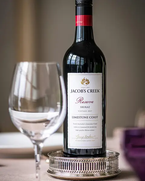 Botella de vino tinto junto a una copa vacía sobre la mesa